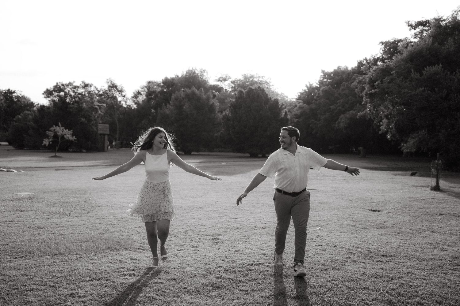 Carefree couple with arms outstretched walking apart playfully in Pretoria Botanical Gardens in black and white photo.