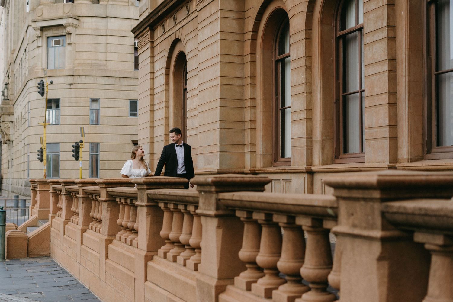 A couple stands on an elegant sandstone balcony in Church Square, Pretoria for their engagement session