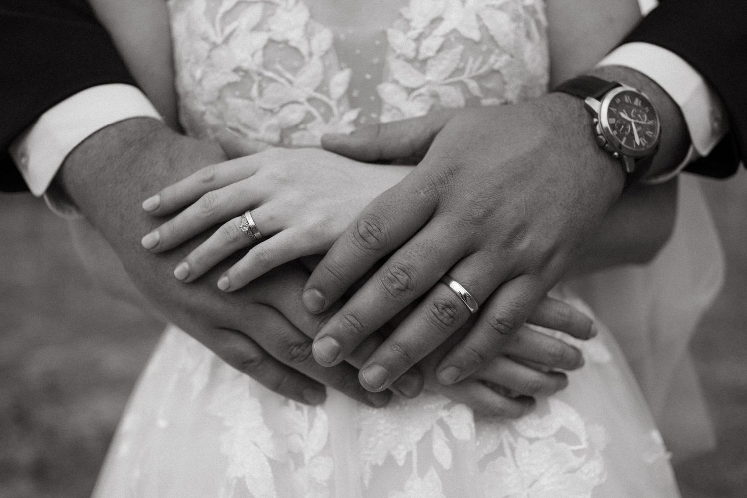 Close-up of newlyweds' hands showing wedding rings against lace dress.