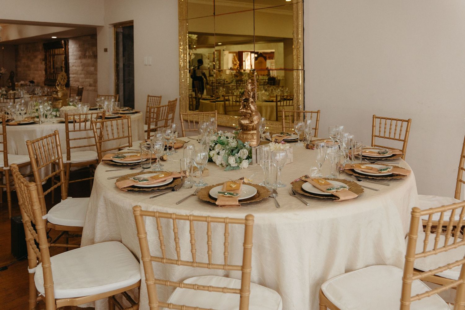 Elegant wedding reception table setting with gold chiavari chairs, white linens, and delicate floral centerpieces.