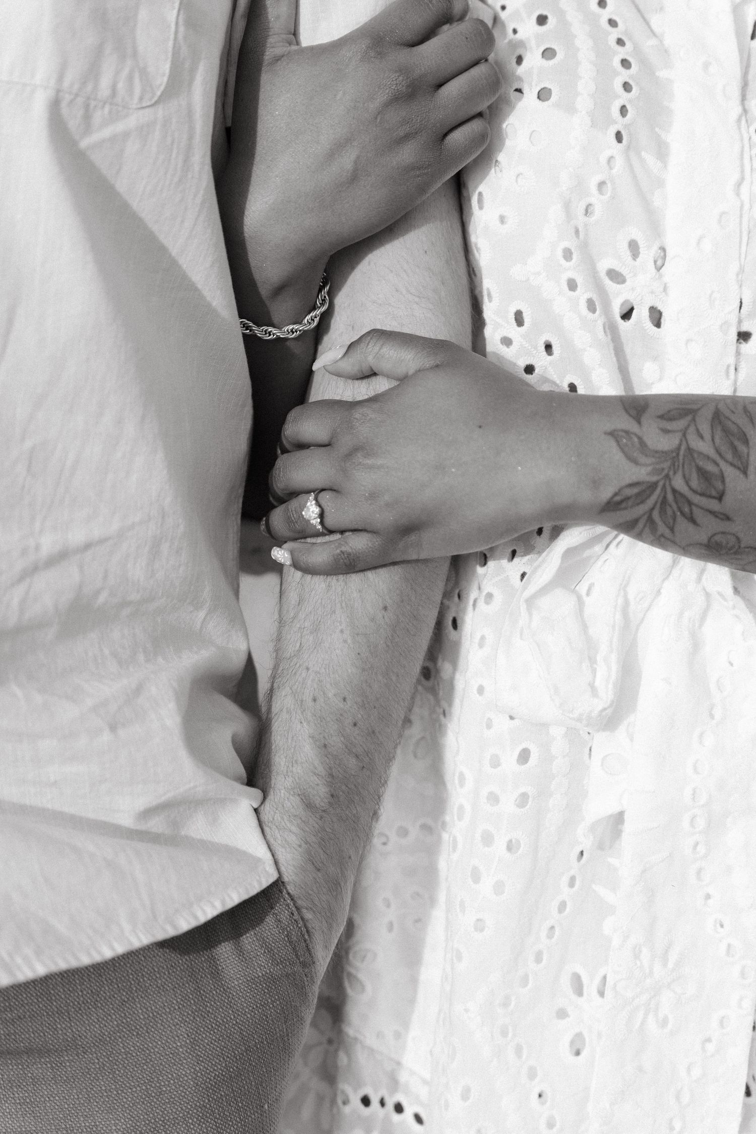Hands gently intertwined in black and white, showing intimate connection against lace curtain background.