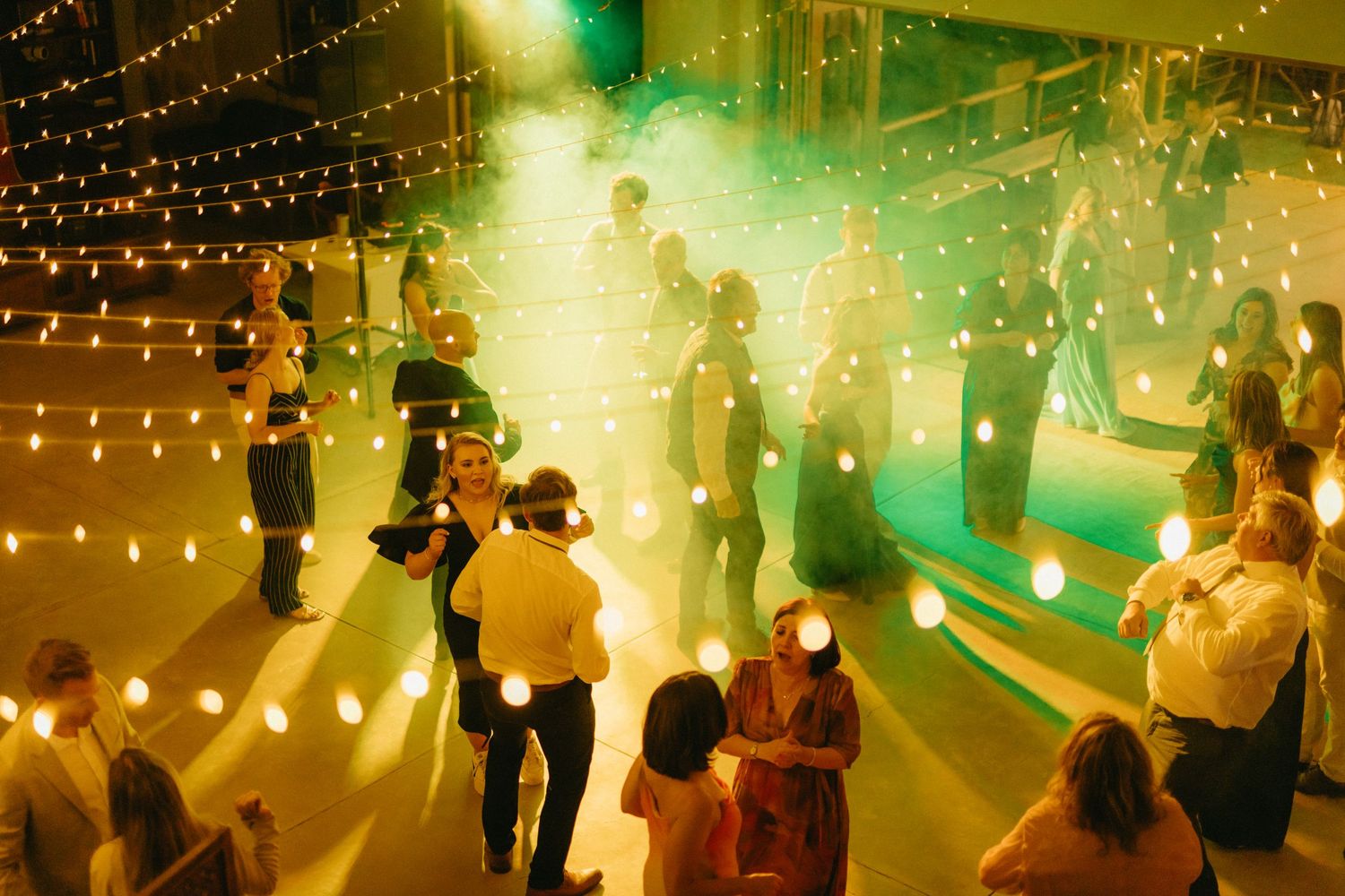 Wedding reception dance floor illuminated with warm string lights and green ambient lighting.