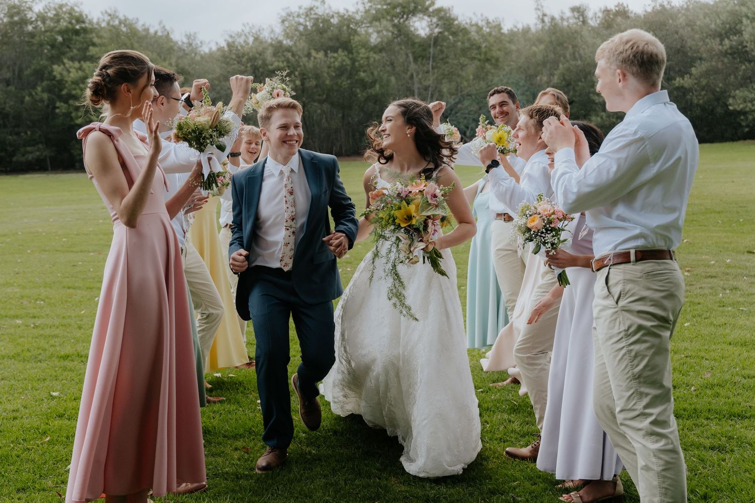 Wedding party celebrates on a sunny lawn with guests in pastel dresses and light suits during an outdoor reception.