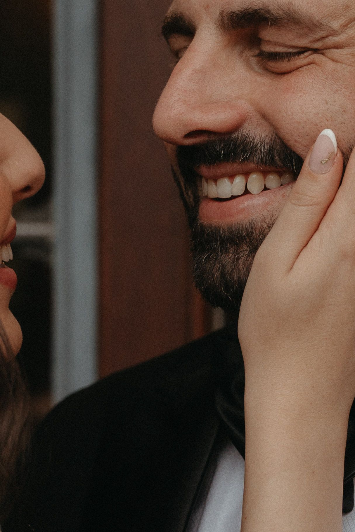 A smiling bearded man being tenderly touched on the cheek by a woman with manicured nails.