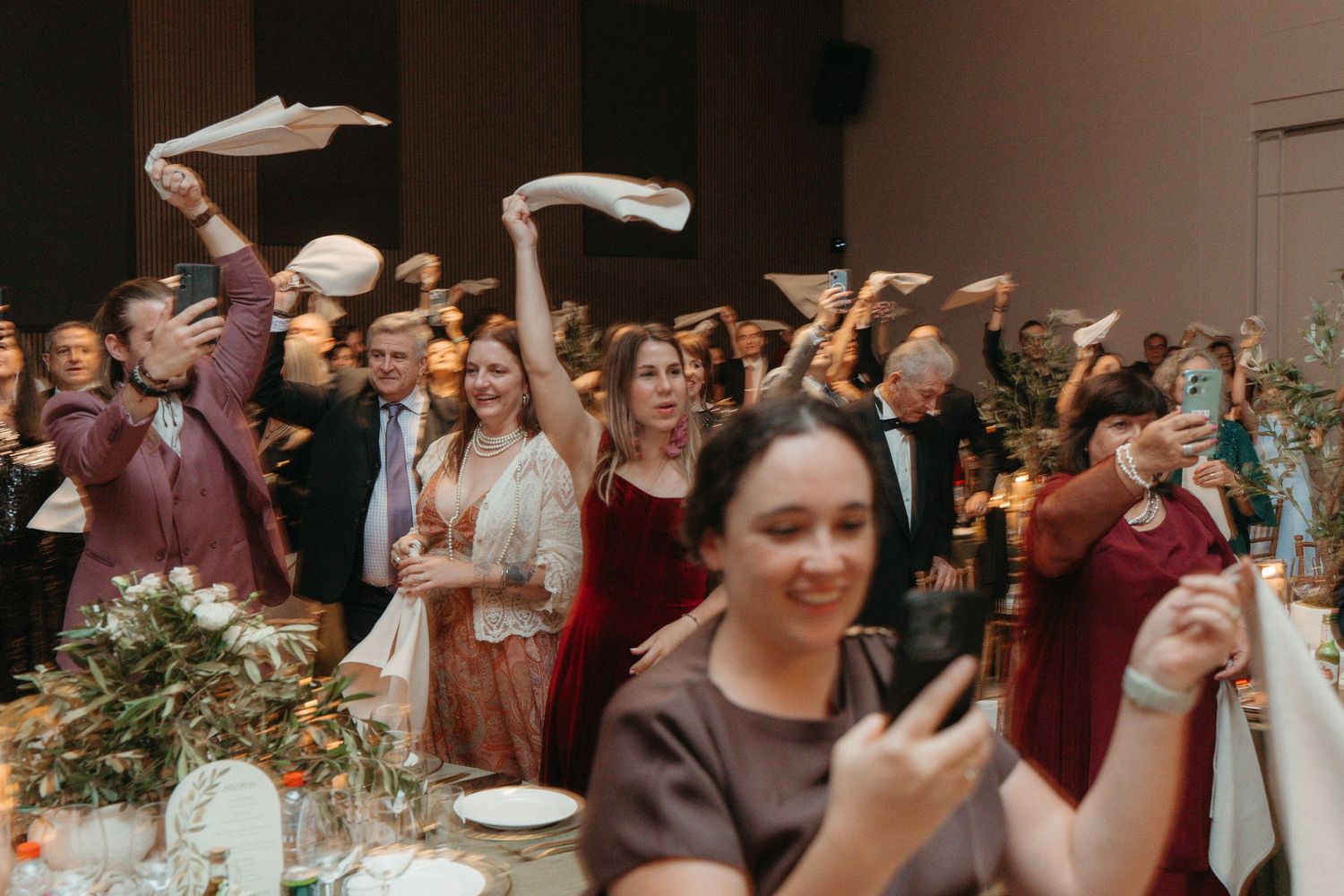 Wedding guests joyfully waving napkins in the air during a lively celebration at an elegant reception venue.