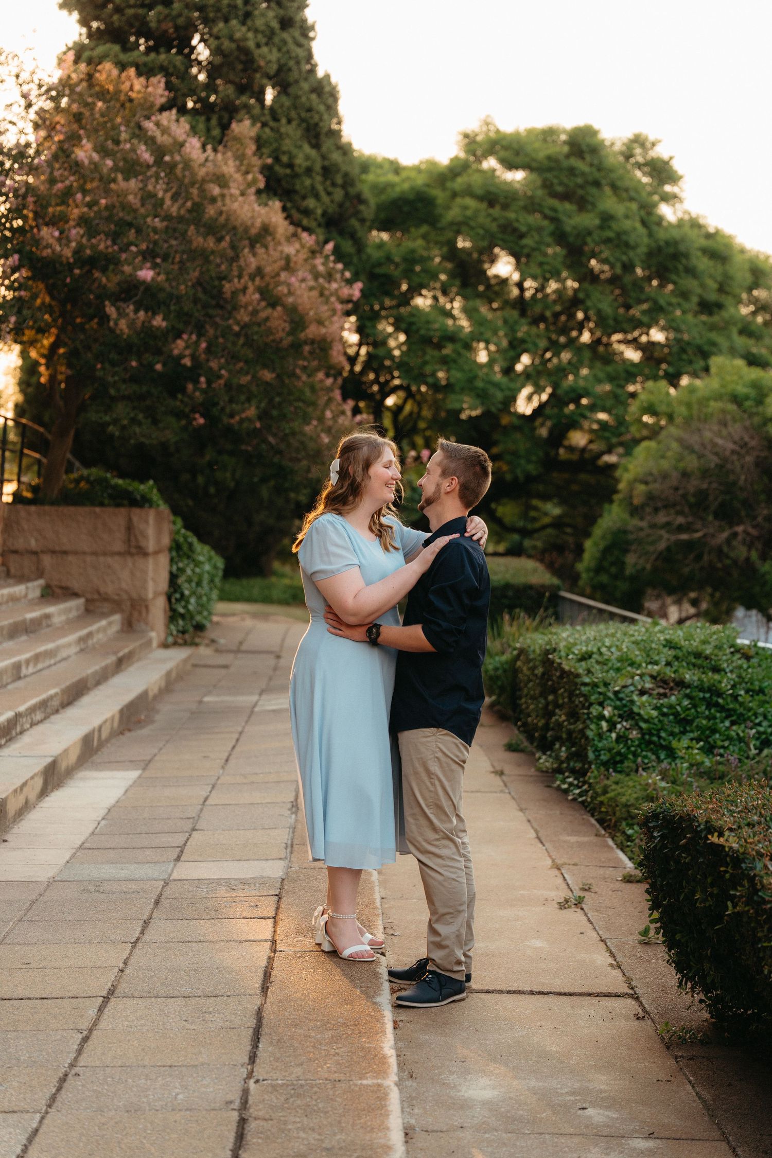Happy couple embracing and laughing on a stone pathway in Johannesburg surrounded by lush gardens at golden hour.