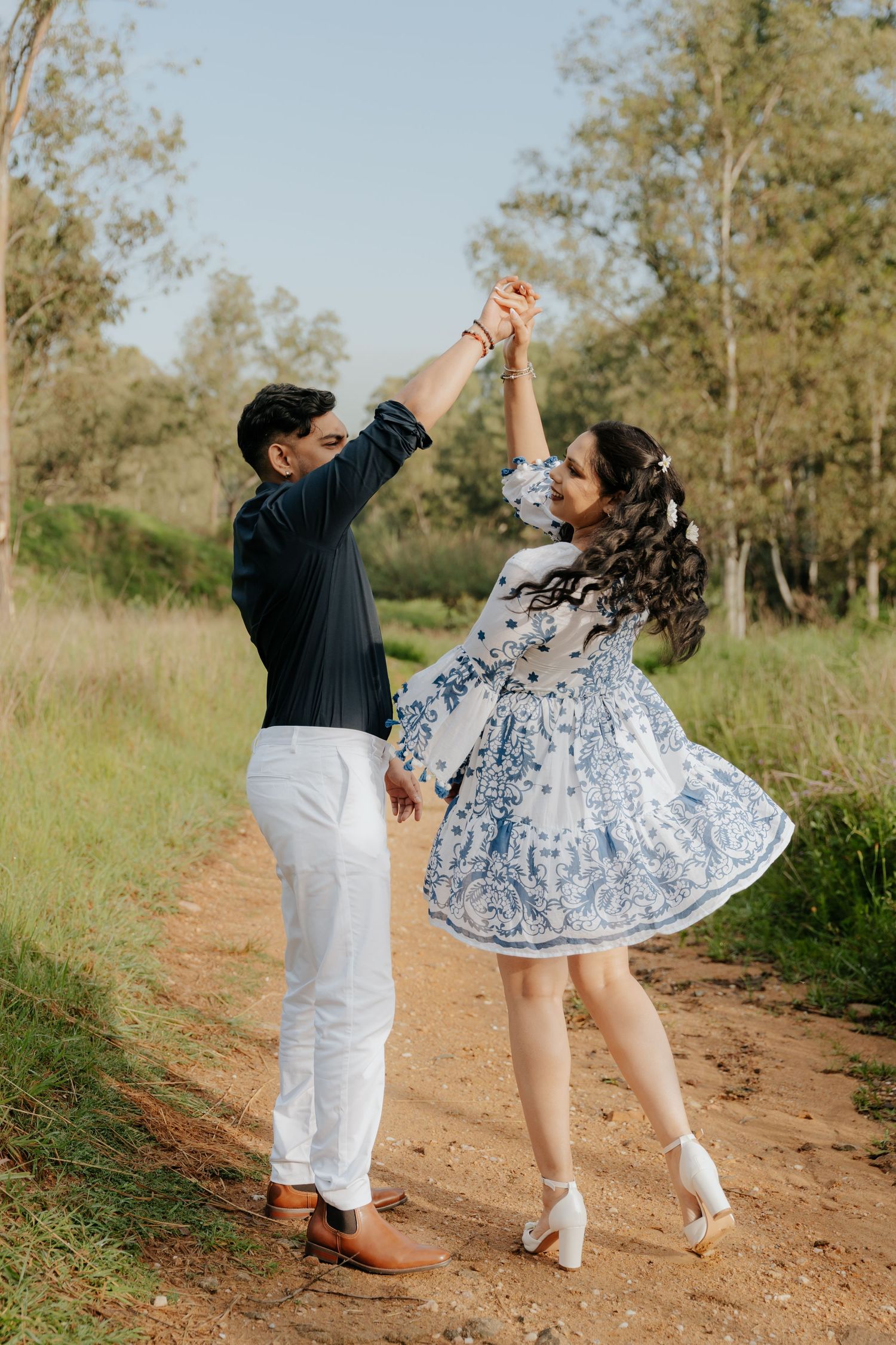 Couple dancing on dirt path in Modderfontein, woman in blue floral dress spinning with arms raised.
