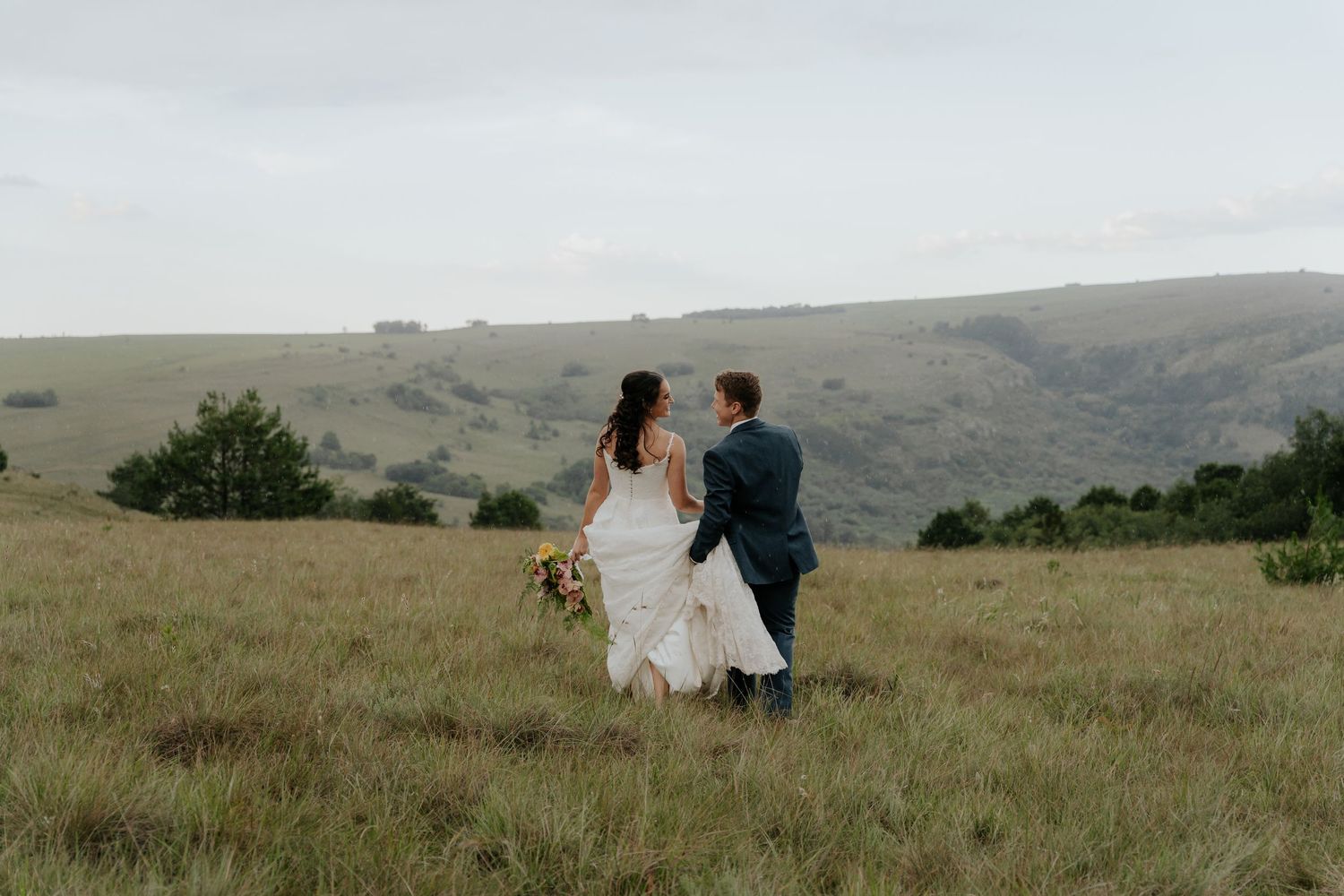 Couple walking together through scenic rolling hills and grassy meadows at sunset.