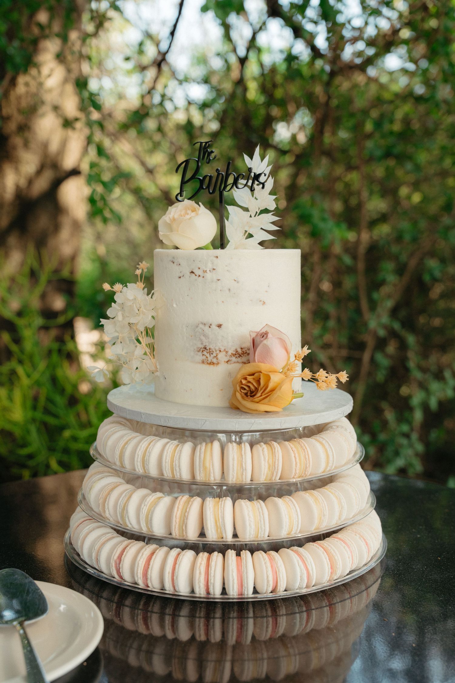 A wedding cake decorated with pink and white macarons arranged in tiers and topped with delicate flowers and a cake topper.