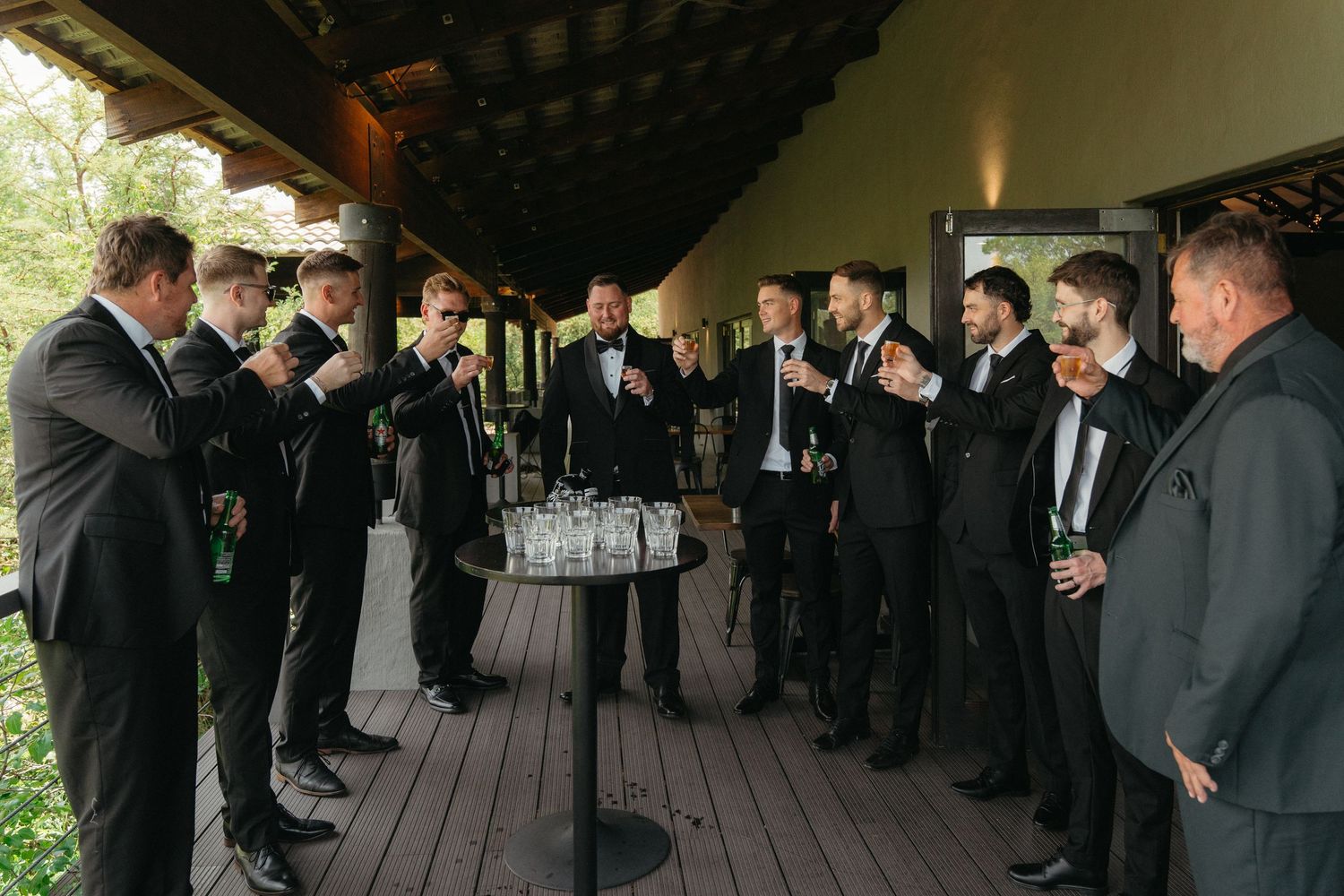 A group of people in formal black attire gather on a wooden deck during a special occasion.