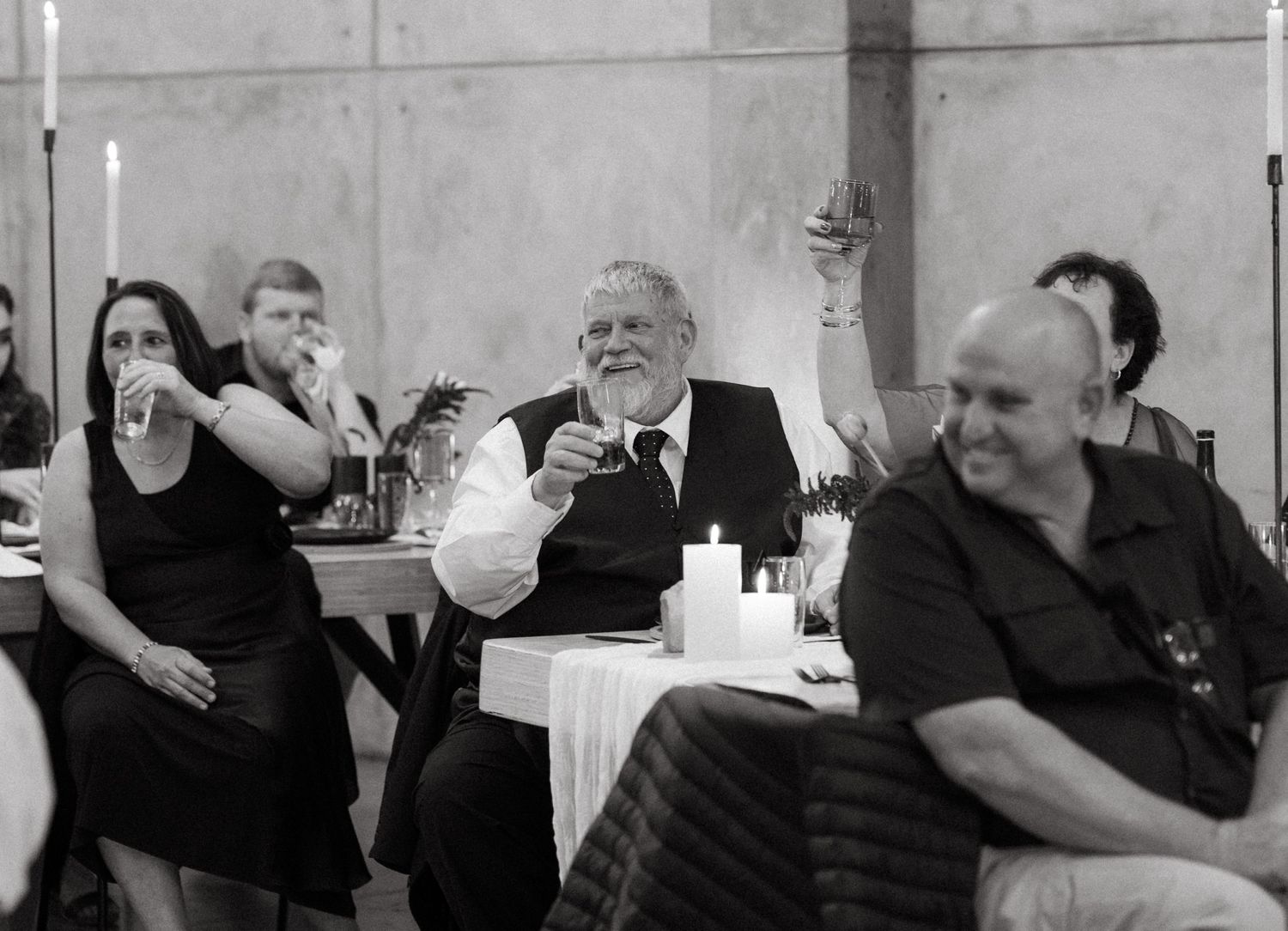 Black and white photo of wedding guests enjoying themselves at a reception table.