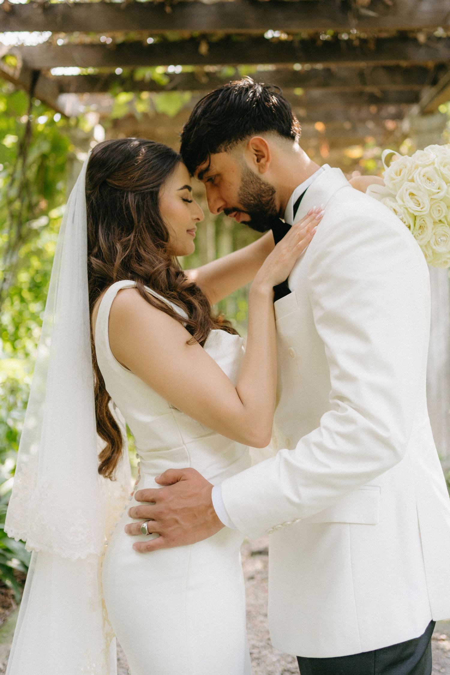 A romantic wedding moment between a couple in white attire sharing an intimate embrace in a garden setting.