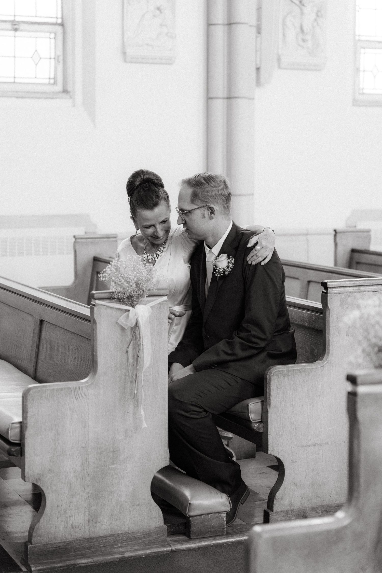 Black and white photo showing two people sharing an intimate moment in church pews at Nazareth House Chapel