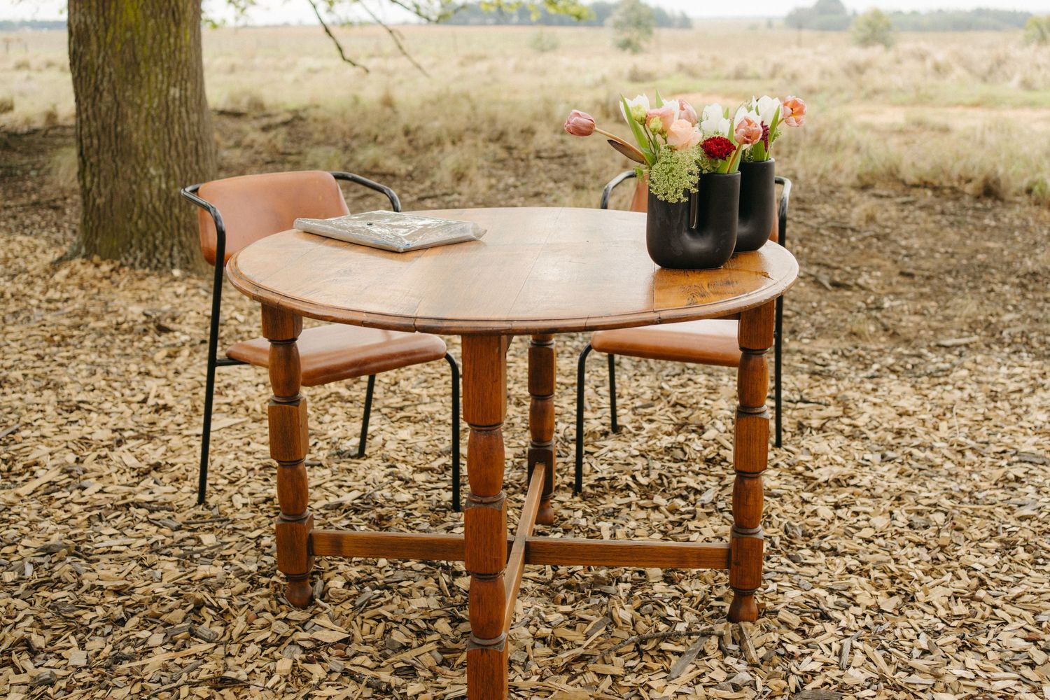 Round wooden table with chairs set up outdoors for rustic event.