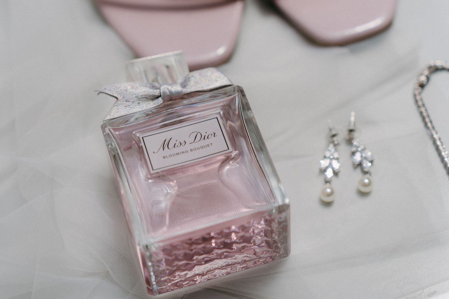 Miss Dior perfume bottle with bridal accessories and jewelry on light surface.