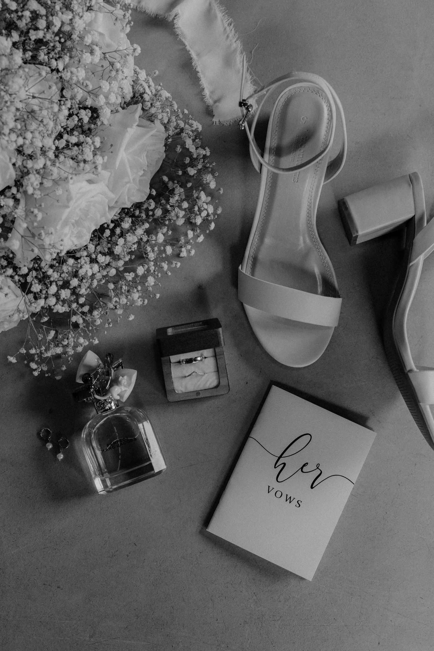 Wedding details flatlay with vow book, flowers, and bridal shoes in black and white.