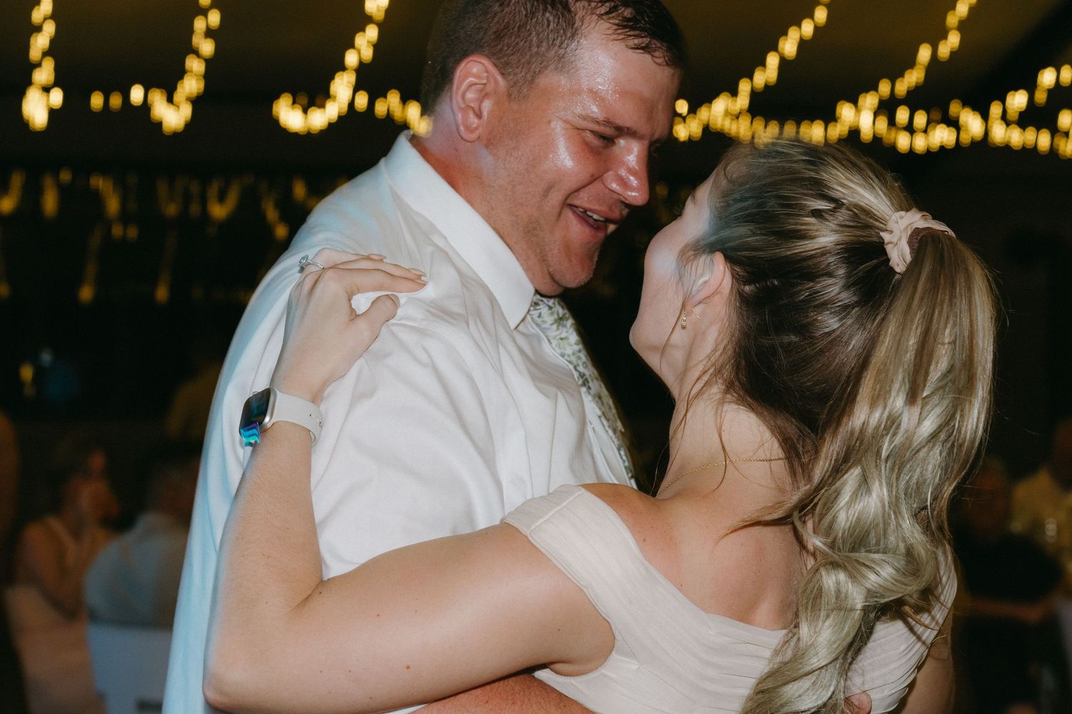 A couple shares an intimate dance moment under twinkling lights at their wedding reception.