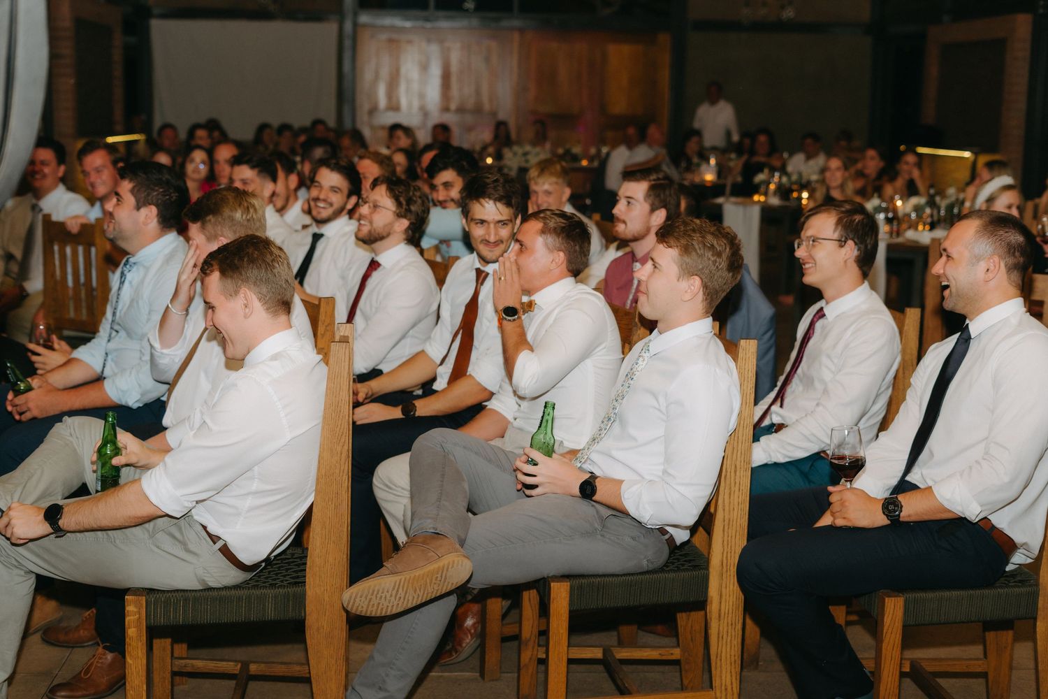 Wedding guests in white shirts and ties seated in rows during the reception.