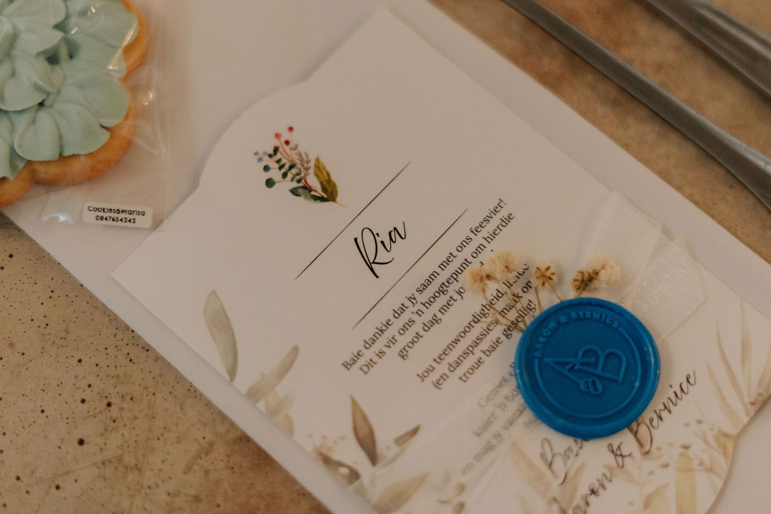 Wedding invitation with blue wax seal and elegant calligraphy on cream-colored paper displayed on marble surface.