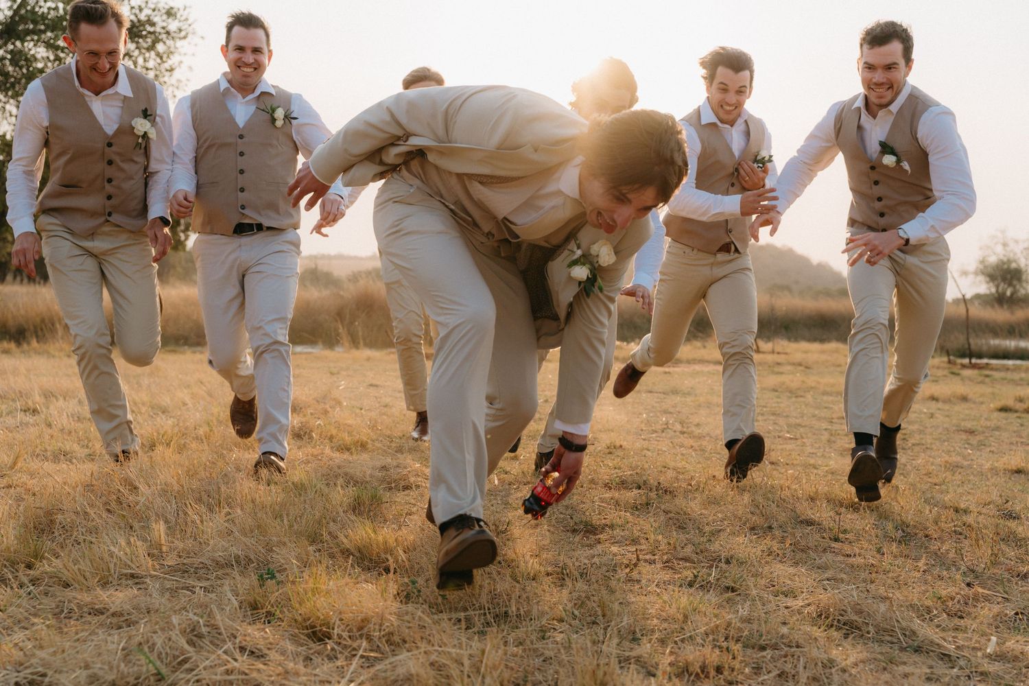 Groomsmen jumping in unison across a field during sunset photo session.