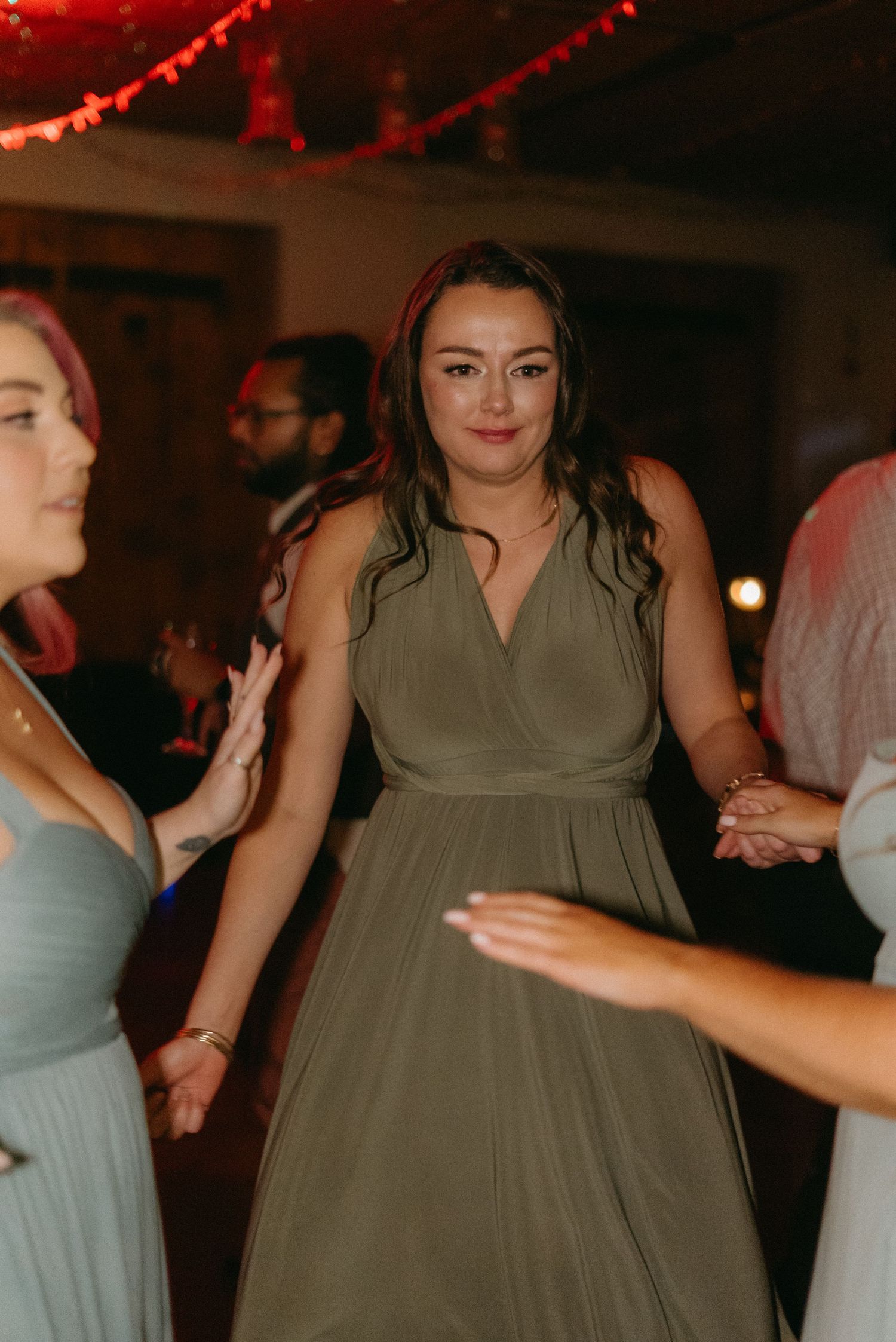 Wedding party members in sage green dresses dance during the reception.