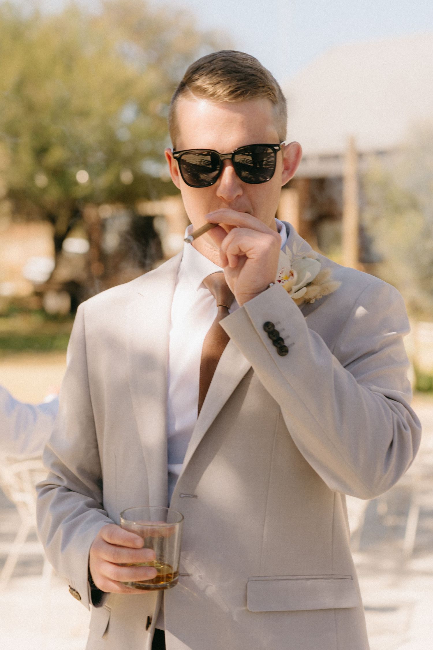 Person in a light colored suit enjoying a drink outdoors during a celebration.