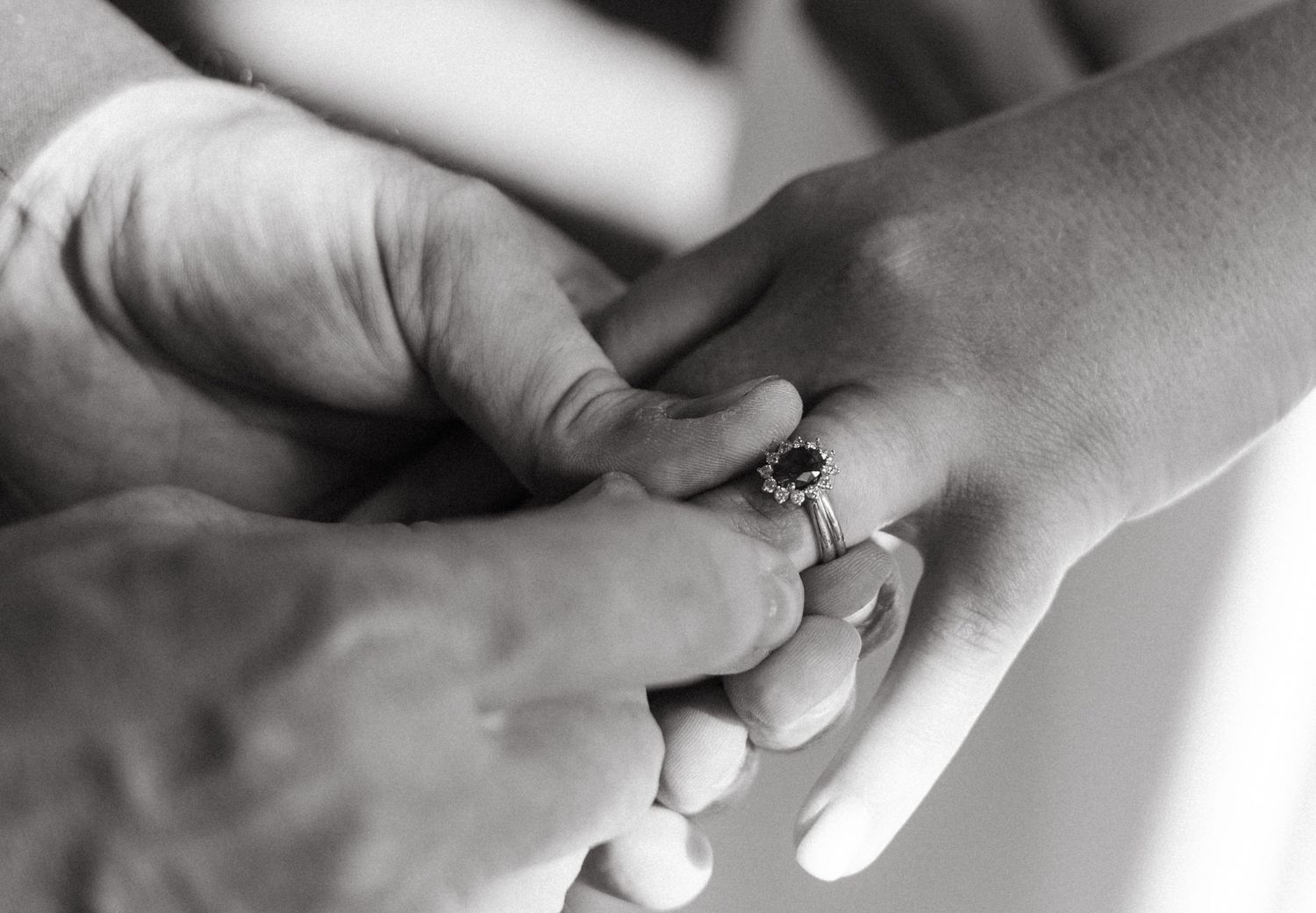Black and white close-up of placing wedding ring on finger during ceremony.