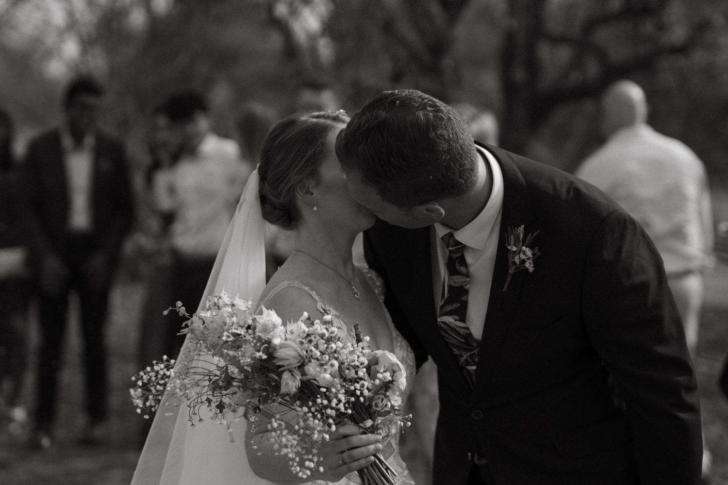 A couple shares an intimate black and white kiss moment during their wedding celebration.
