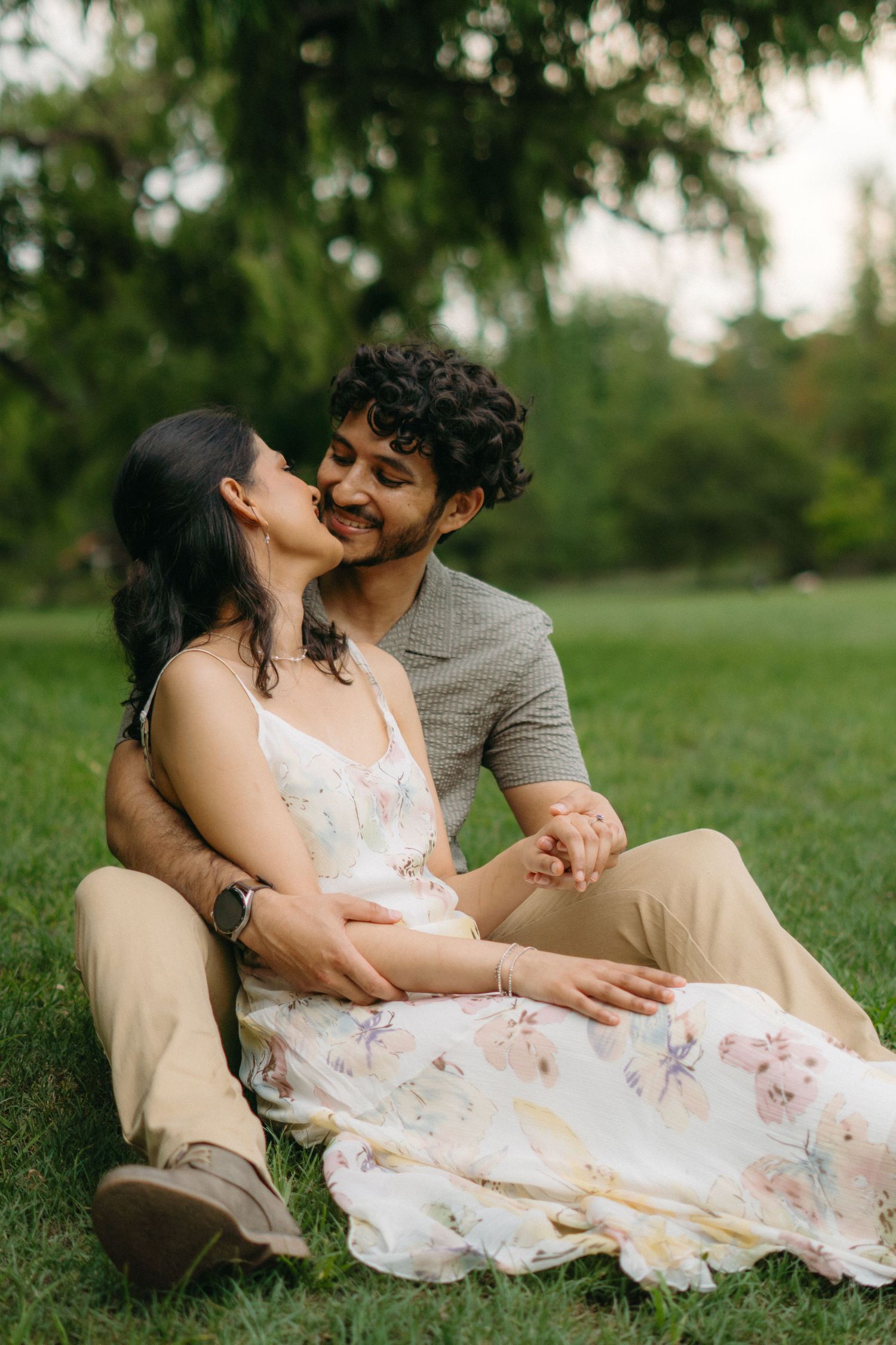 A couple shares a joyful moment while sitting together on grass in a park.