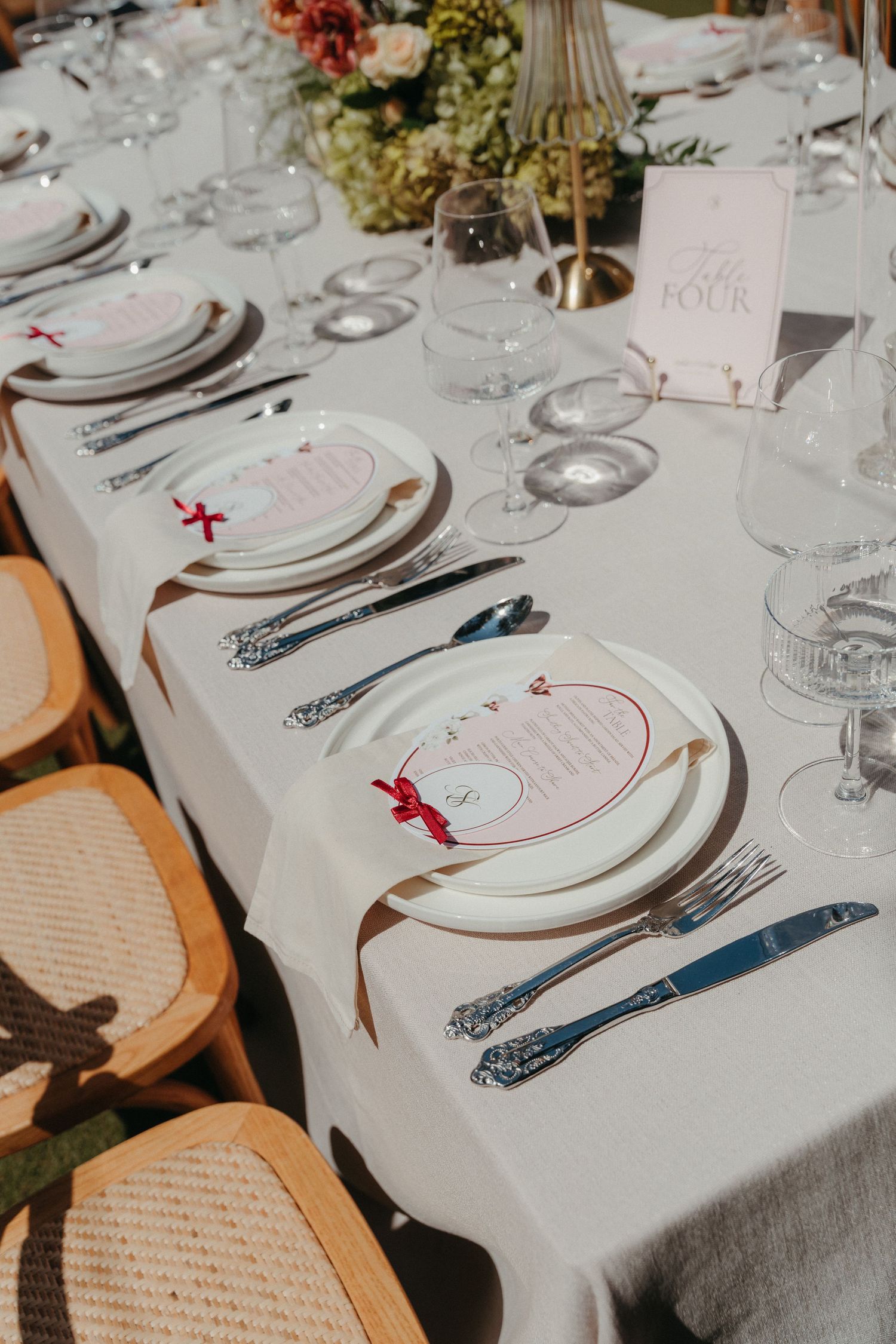 Elegant wedding table setting with white plates, silver cutlery, crystal glasses, and floral centerpieces on a white tablecloth.