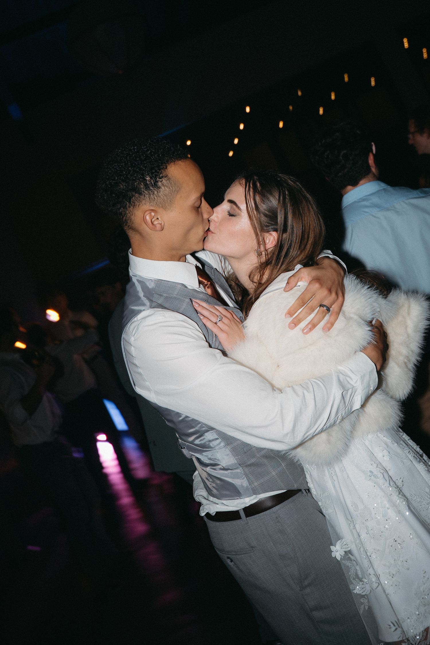 A couple shares a romantic first dance kiss at their wedding reception, with the bride in a white dress and fur wrap.