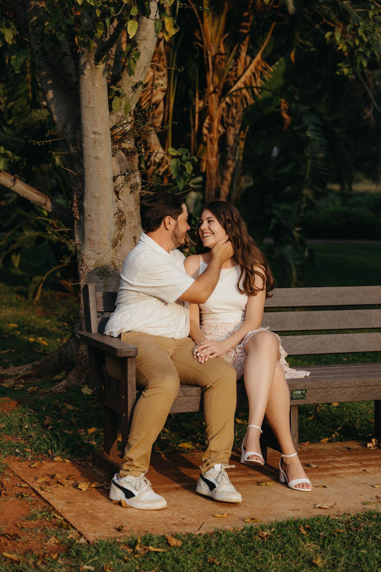 Romantic couple sitting close together on a wooden park bench smiling at each other outdoors.