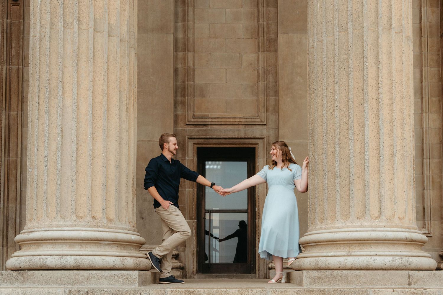 A person in a blue dress twirls between classic stone columns at Wits Great Hall, Johannesburg