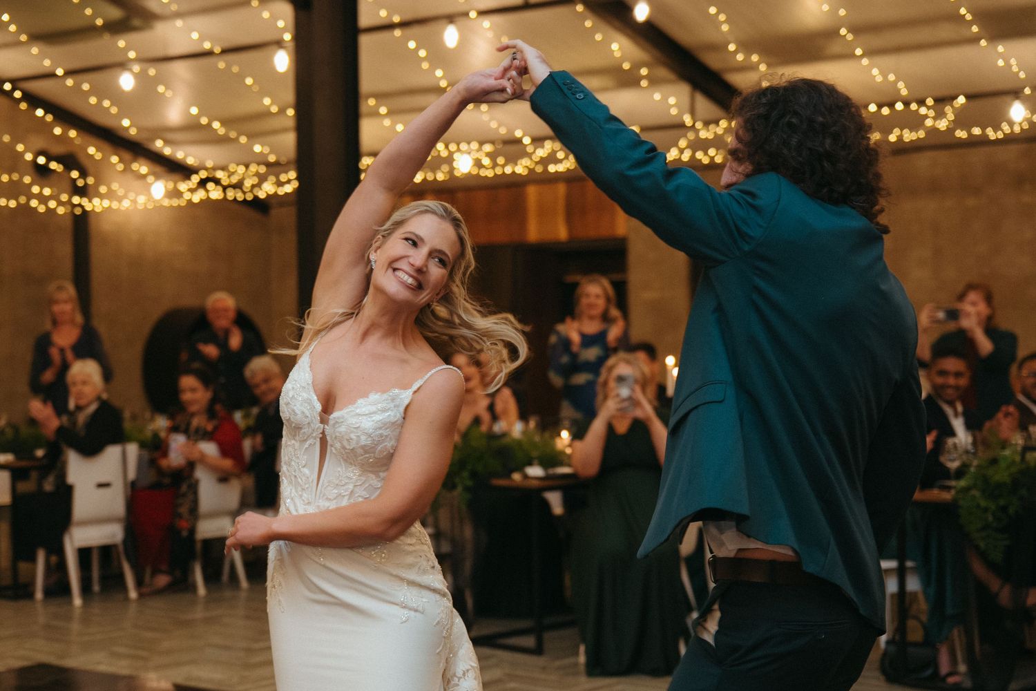 Bride in lace wedding dress twirling during first dance under warm string lights at reception at Rosemary Hill Farm