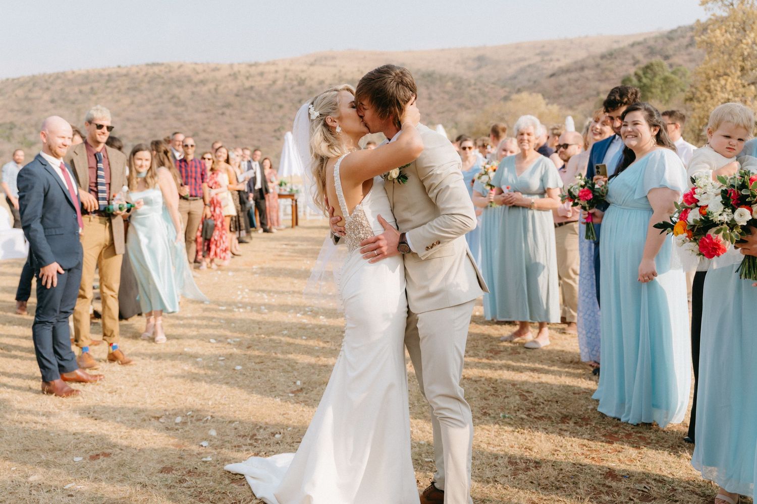 Wedding party in light blue bridesmaid dresses gathers outdoors in a rustic mountain setting for celebration photos.