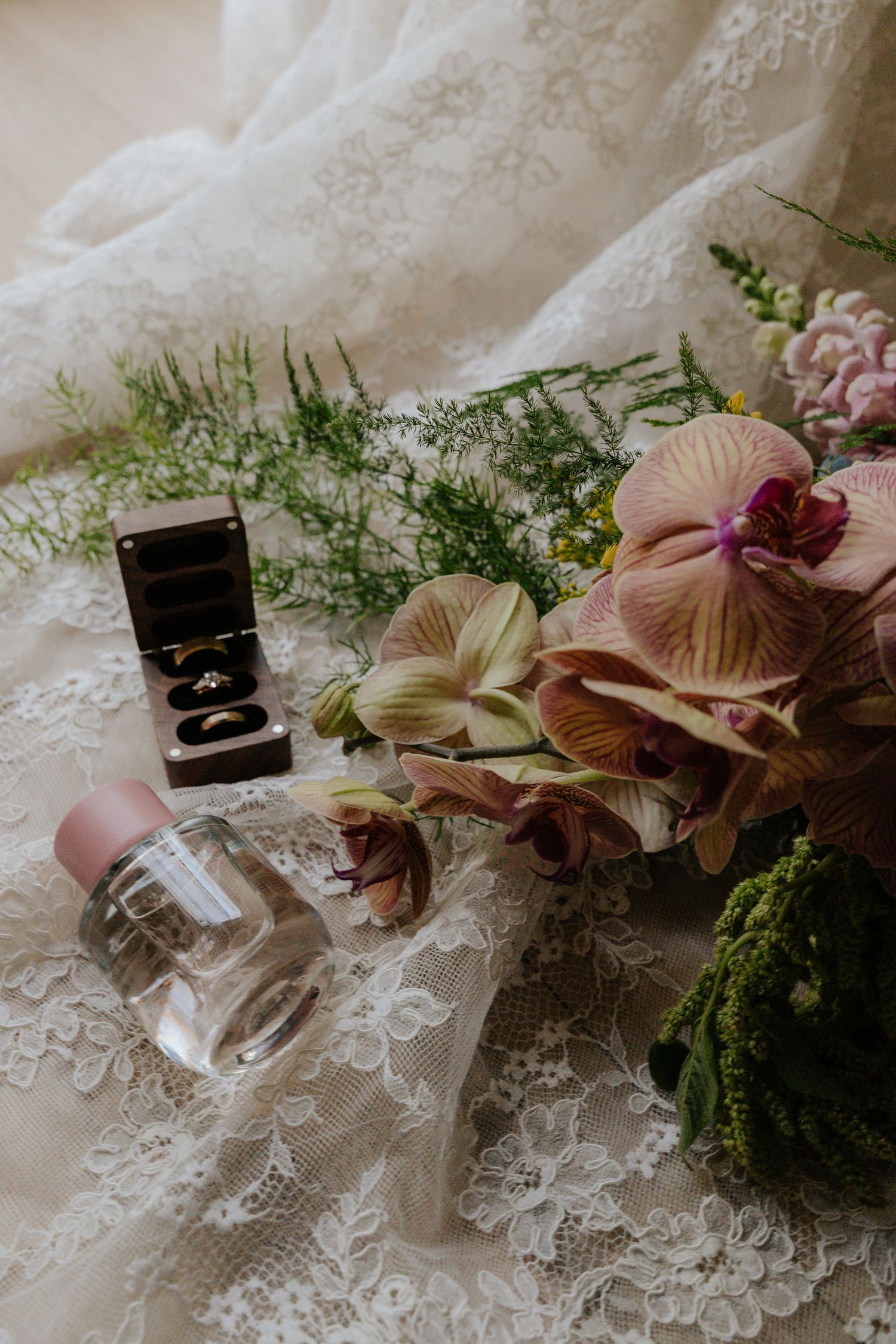 Vintage perfume bottle and delicate pink flowers arranged on white lace fabric with greenery accents create a romantic still life.