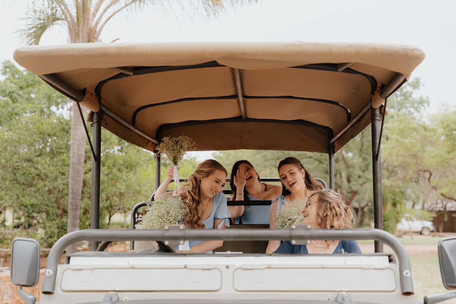 Wedding party riding in a covered golf cart through a sunny outdoor venue.