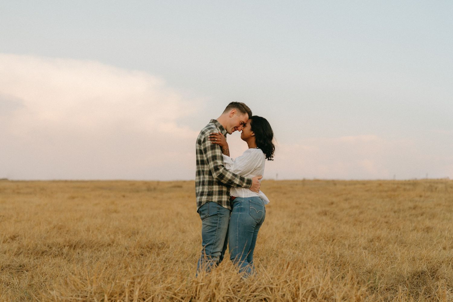 Couple walking together through a vast golden wheat field on a bright sunny afternoon.