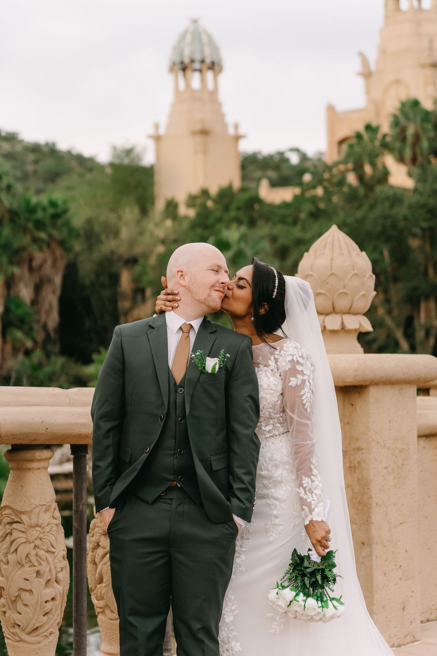A romantic outdoor wedding moment at a venue with Mediterranean-style architecture and towers in the background.