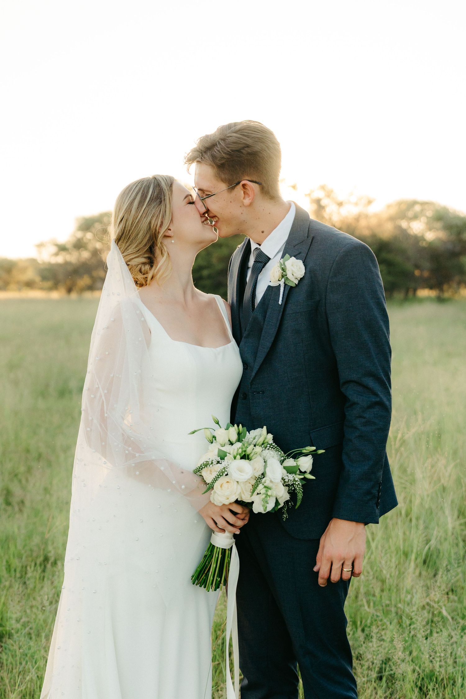 Intimate wedding portrait of newlyweds sharing a romantic moment in a sunlit field.