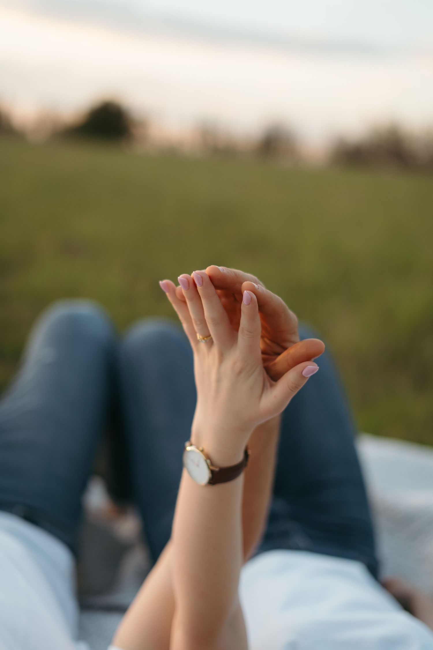 Close-up shot of intertwined hands with a watch against a blurred outdoor background at sunset.