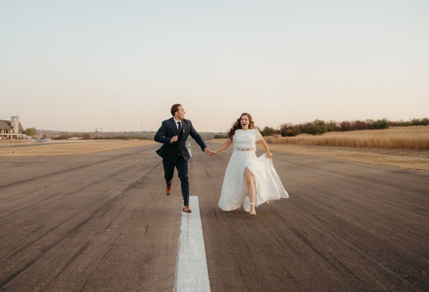 Joyful couple running down the center line of an empty runway.