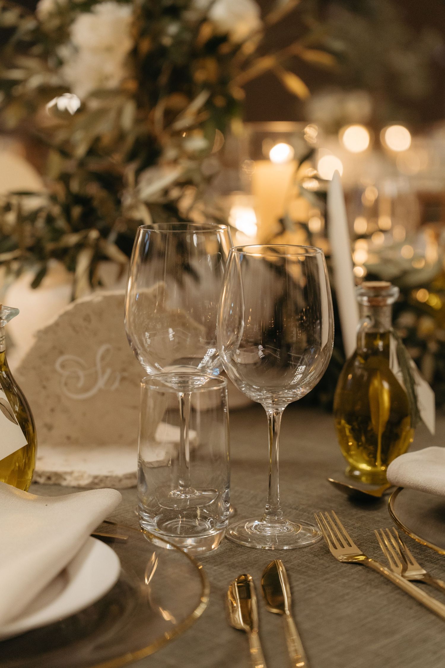 Elegant table setting with crystal wine glasses, gold cutlery, candles, and floral centerpiece for a formal dinner.
