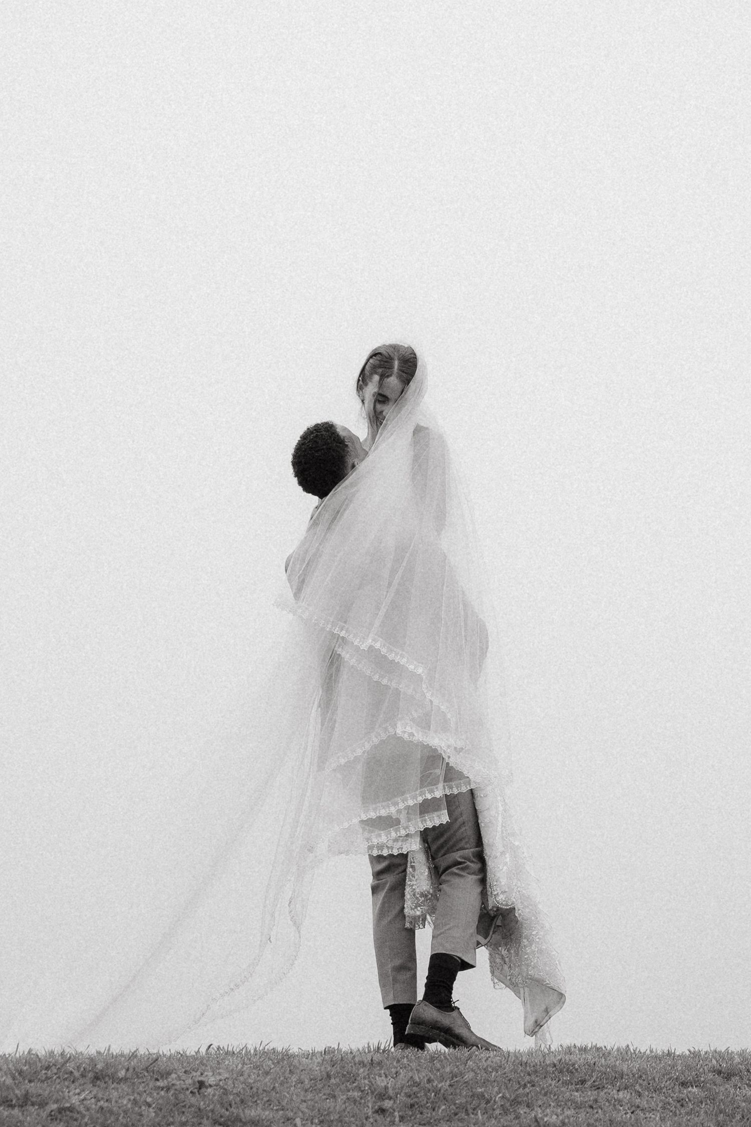 Black and white photo of a groom lifting his veiled bride in a misty outdoor setting in the Western Cape