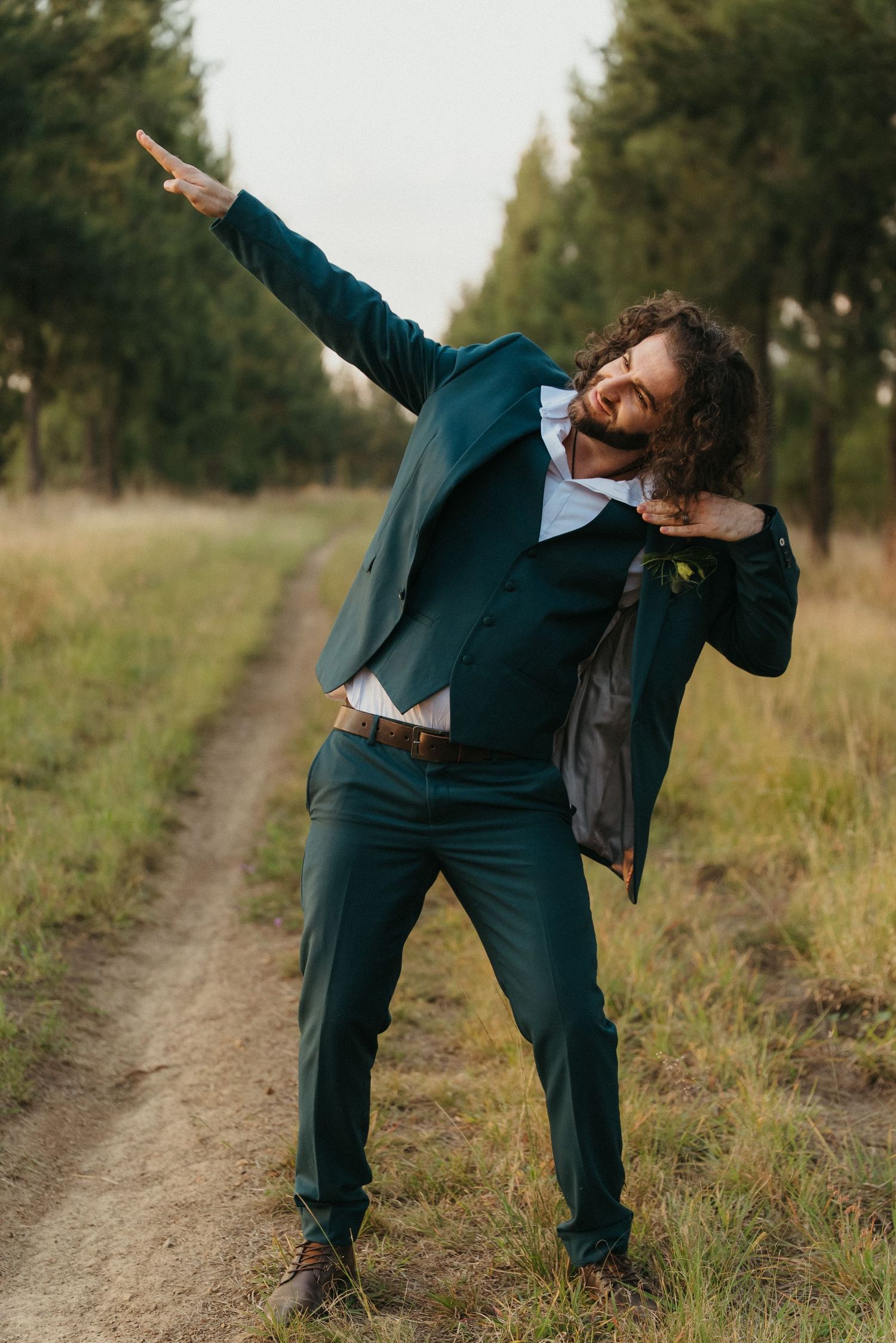 Man in teal suit dabbing on a rural dirt path surrounded by trees and grassland.