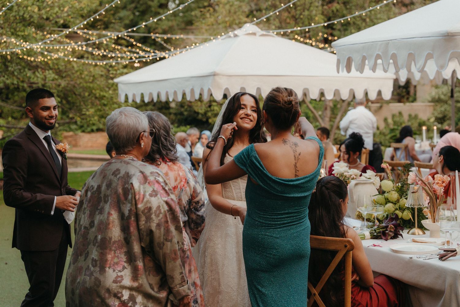 Bride greeting guests at outdoor wedding reception under string lights near white tent.