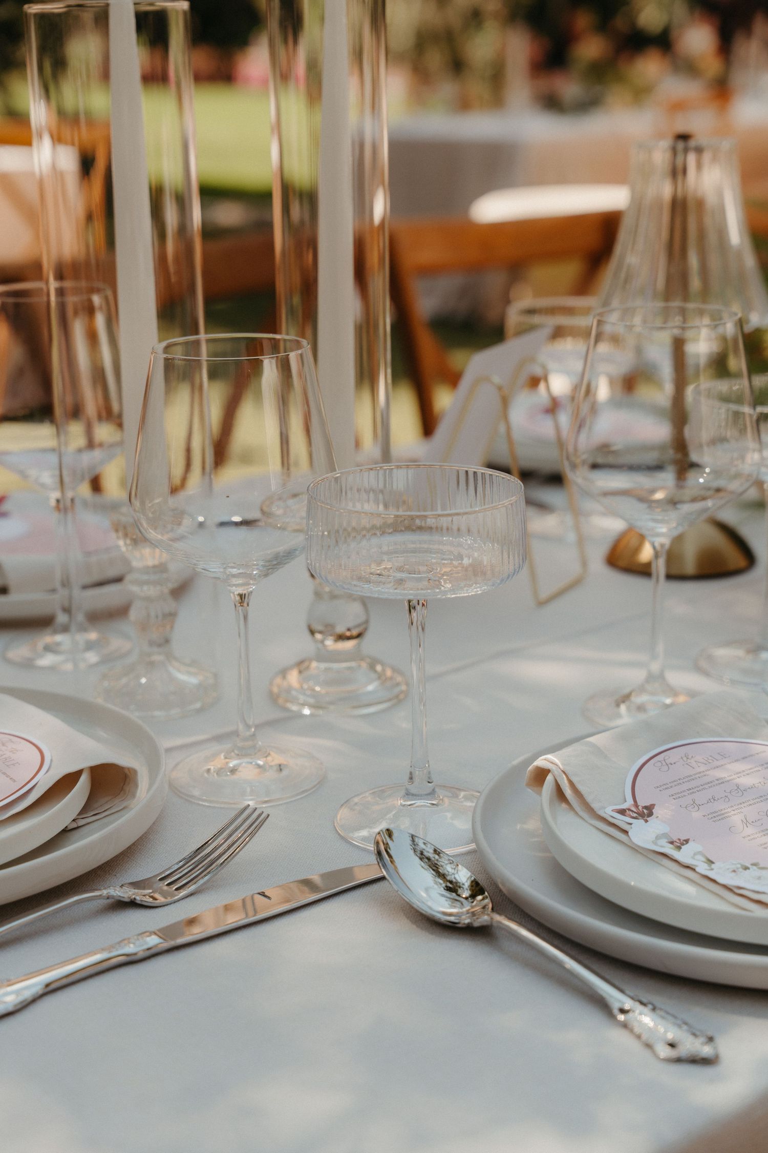 Elegant wedding table setting with crystal glassware, silver cutlery, and white plates on a linen tablecloth.
