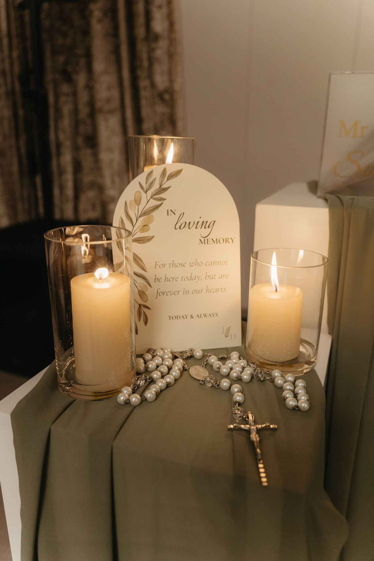 In loving memory display with lit candles, rosary beads, and a cross on a draped table at a wedding reception.