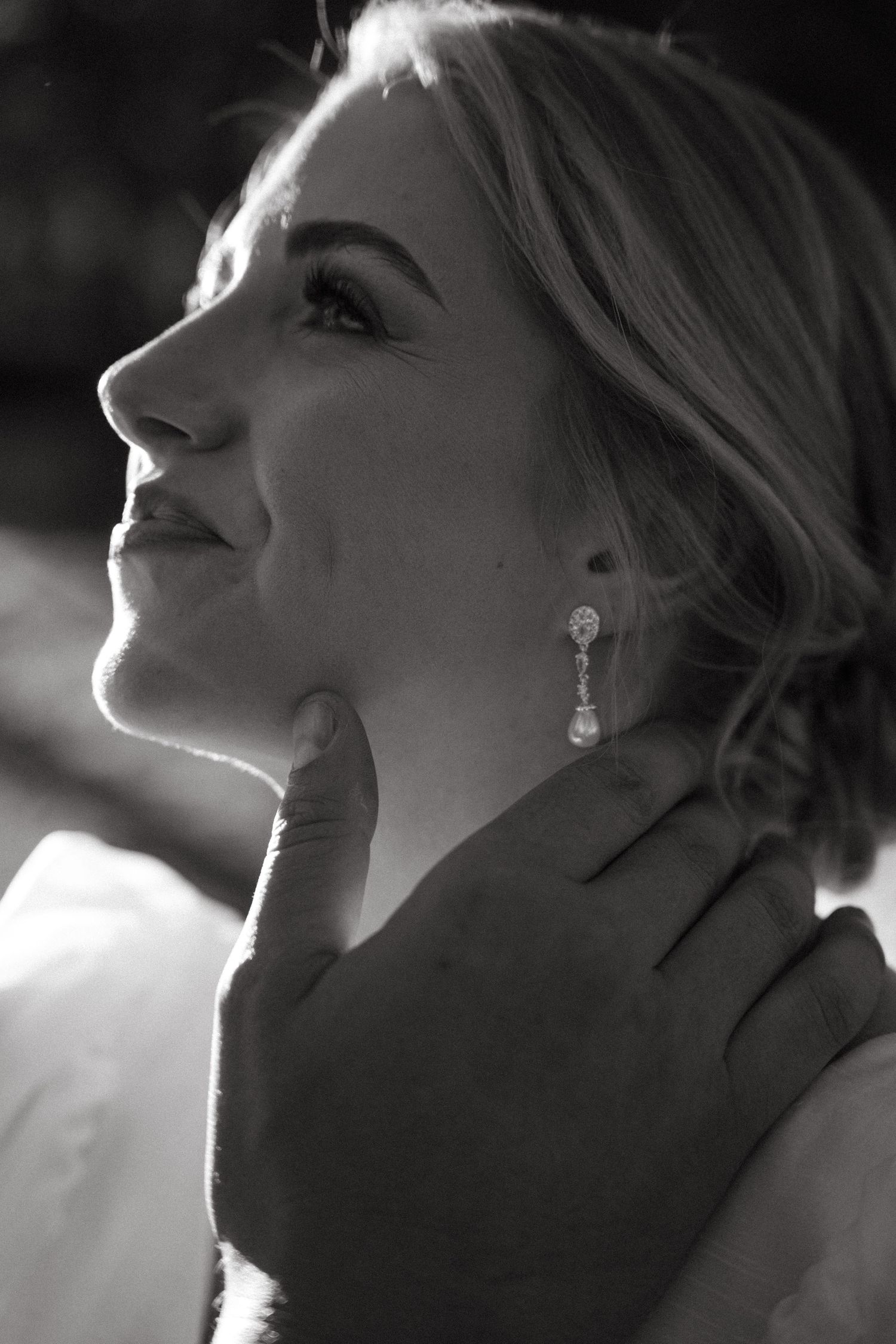 Black and white close-up portrait of radiant bride wearing elegant drop earrings with gentle hand on chin in Rustenburg, South Africa