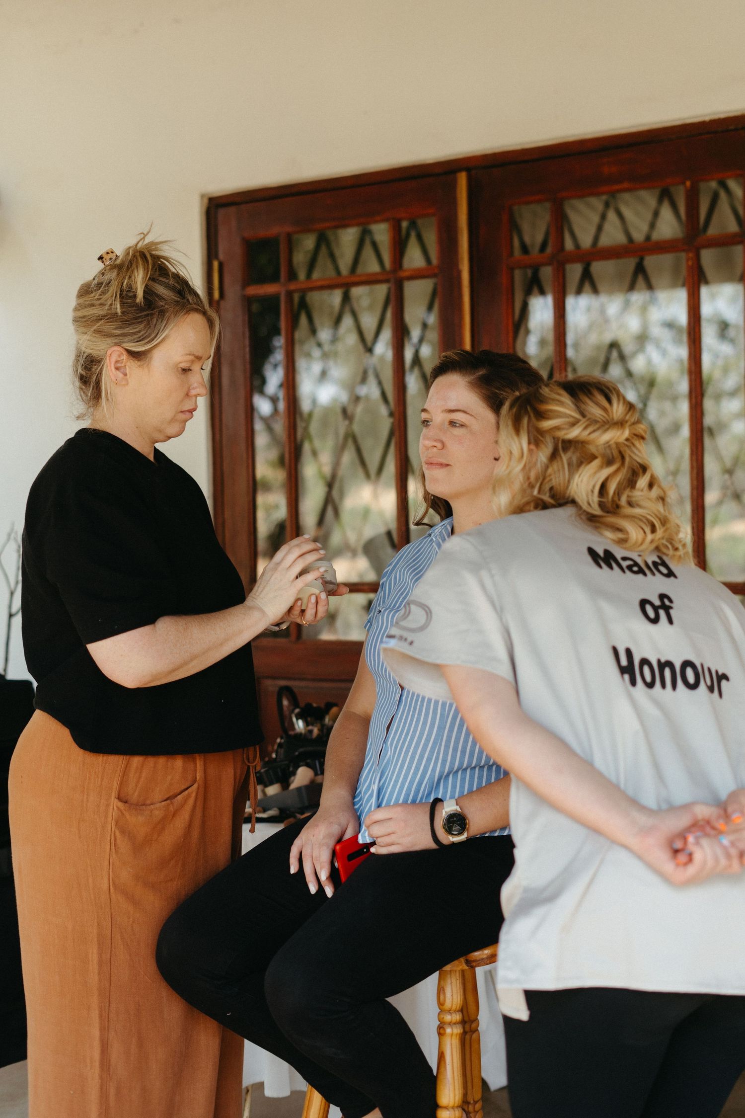 Wedding preparation scene with styling and makeup being done in front of vintage windows.